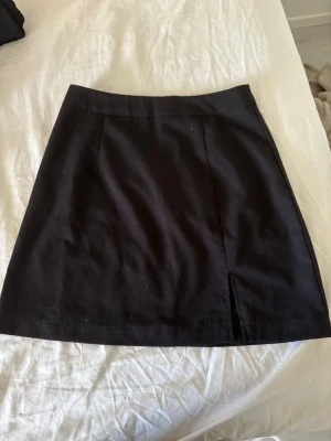 Svart kortkjol från Pieces - Snygg svart kortkjol från Pieces med enkel och stilren design. Kjolen har en liten slits framtill och stängs med dragkedja bak. Perfekt att matcha med en crop top eller stickad tröja för en trendig look.