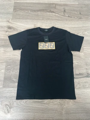 Svart Fendi t-shirt med logga - Svart t-shirt från Fendi med korta ärmar och en guldfärgad broderad Fendi-logga på bröstet. Klassisk passform och rund halsringning. Perfekt för dig som gillar exklusiva märken och stilren design.