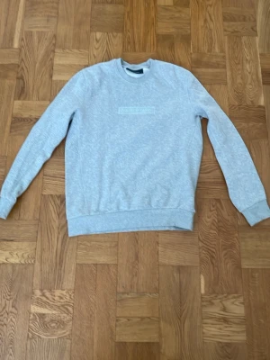 Grå sweatshirt från Peak Performance - Snygg grå sweatshirt från Peak Performance med broderad logga på bröstet. Klassisk rund halsringning och ribbade muddar vid ärmslut och nederkant. Knappt använd och nypris cirka 500kr