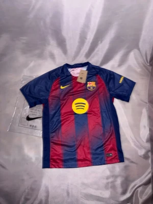FC Barcelona matchtröja Nike - Säljer en FC Barcelona matchtröja från Nike i klassiska blå och röda färger med gula detaljer. Tröjan har klubbmärke, Nike-logga och Spotify-logga på bröstet. Korta ärmar och sportig passform, perfekt för fotbollsträning eller support.
