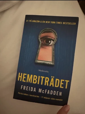 Hembiträdet av Freida McFadden - Spännande roman med blått omslag och ett öga som tittar genom ett nyckelhål. Boken är skriven av Freida McFadden och utgiven av Modernista. Perfekt för dig som gillar thrillers och mysterier.
