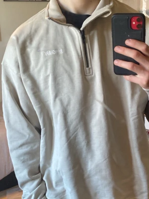 Beige Gymshark Quarter zip med dragkedja - Snygg beige tröja från Gymshark med 1/4 dragkedja framtill och broderad logga på bröstet. Tröjan har ribbade muddar vid ärmslut och nederkant. Perfekt för en sporting och avslappnad stil. Kommer med original förpackning. Öppnad men aldrig använd. Alltså inga tecken på användning (Jag har en smutsig spegel). Storlek: Small, Oversized fit.