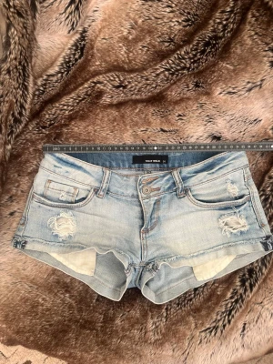 Ljusblåa jeansshorts från Only Wear - Säljer ett par ljusblåa jeansshorts från Only Wear med slitna detaljer och råa kanter. Shortsen har klassisk femficksdesign, knapp- och dragkedjestängning samt låg midja. Perfekta för varma dagar och en avslappnad stil.