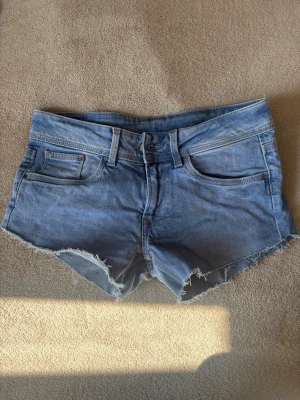Blå jeansshorts pepe jeans - Snygga blå jeansshorts med fransig, rå kant och klassisk femficksdesign. Shortsen har bälteshällor och knappgylf. Perfekta för varma dagar och en avslappnad stil.