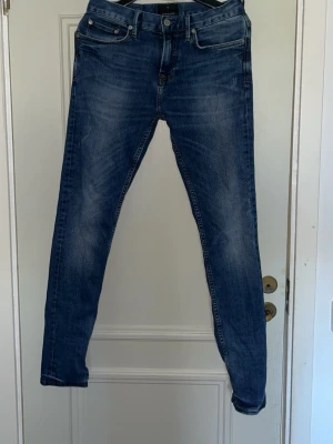 Blå slim fit jeans med slitningar - Snygga blå slim fit jeans med lätt slitna detaljer och klassisk femficksdesign. Jeansen har normal midja och smala ben, perfekt för en trendig och avslappnad look. Materialet är mjukt och stretchigt för extra komfort.