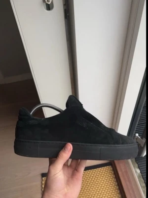 Svarta mockasneakers med låg profil - Stilrena svarta sneakers i mocka med helsvart sula och klassisk låg siluett. Perfekta för en clean och minimalistisk look. Skon har rund tå och diskreta sömmar för en enkel men snygg design.