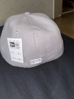 Grå New Era 59FIFTY keps - Snygg grå keps från New Era 59FIFTY-serien, tillverkad i 100% polyester. Klassisk fitted-modell med broderad logga baktill och Cooperstown Collection-märke på insidan. Perfekt för dig som gillar streetwear och sportig stil.
