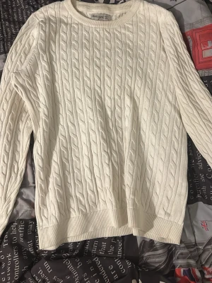 Vit kabelstickad tröja - Kabelstickad vit tröja från Basic Spirit med rund halsringning och ribbade muddar vid ärmslut och nederkant. Klassisk och enkel design som passar till det mesta. Tillverkad i mjukt material för extra komfort.