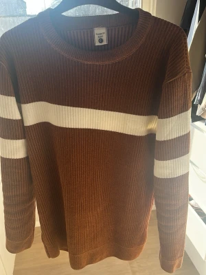 Brun ribbad tröja med vita ränder - Snygg brun ribbad tröja från Fashion Basic med vita horisontella ränder över bröstet och på ärmarna. Tröjan har rund halsringning och långa ärmar. Perfekt för dig som gillar retrovibbar och vill ha en bekväm och stilren look. Storlek L funkar som M. Nypris 1200kr