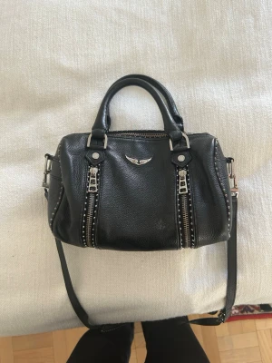 Zadig Voltaire väska - Zadig Voltaire sunny handväska. Är osäker på exakt vilken storlek men det är inte den minsta utan den som är lite större. Svart liten Zadig väska med silverdetaljer. Den är lite sliten på vissa ställen men inte sönder eller så. Kan tänka mig att gå ner i pris vid snabb affär.