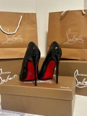  Louboutin klackar - Säljer ett par ikoniska svarta pumps från Christian Louboutin i glansigt lackläder med klassisk röd sula och spetsig tå. Skorna har en hög stilettklack som ger en elegant och edgy look. Perfekta för dig som vill sticka ut med exklusiv design. 