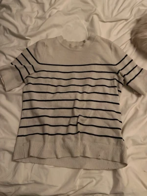 Vit och marinblå randig topp - Kortärmad topp i vit med marinblå horisontella ränder. Rund halsringning och ribbade kanter vid ärmslut och nederkant. Perfekt till jeans eller kjol för en avslappnad look.