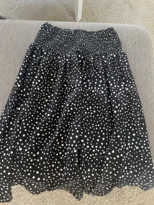 Svart prickig kortkjol med resårmidja - Säljer en svart kortkjol med vita prickar och bred smockresår i midjan. Kjolen har en luftig passform och är gjord i ett luftigt tyg som ger ett snyggt fall. Perfekt för dig som gillar trendigt mönster och vill ha en bekväm kjol till sommaren. (Pris går att diskutera)🫰