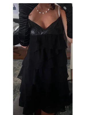 Svart volangklänning med paljetter - Svart kortklänning med volanger och paljettprydd överdel. Klänningen har smala axelband och en v-ringad urringning. Perfekt för dig som vill sticka ut med en glittrig och elegant look. Det är en underbar klänning som tyvärr inte riktigt passar mig och därför väljer jag att lägga ut!✨🪻