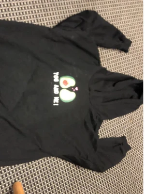 Svart t-shirt med avokadotryck - Cool svart t-shirt med ett gulligt tryck av två avokadohalvor och texten 'You and me!'. Perfekt för dig som gillar roliga motiv och vill sticka ut lite extra. T-shirten har korta ärmar och är tillverkad i mjuk bomull.