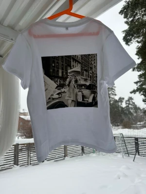Vit t-shirt med ett unikt retro tryck på ryggen - Snygg vit t-shirt med ett stort svartvitt retro fototryck på ryggen som ger en cool vintagekänsla. Klassisk rund hals och korta ärmar. Perfekt för dig som gillar streetstyle och vill sticka ut lite extra.