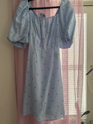 VERO MODA klänning med puffärm strl S - Söt blå kortklänning med små röda körsbärsmönster och tunna vita ränder. Klänningen har puffiga kortärmar och en rak, något utställd passform. Perfekt för sommarens alla tillfällen och ger en romantisk vibe. Storlek S. Endast använd en gång så i nyskick. Bilden : 178 cm lång och klänningen slutar precis ovanför knäna 