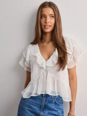 Vit volangblus med v-ringning - Söt vit blus med volanger och djup v-ringning. Blusen har korta ärmar med volangdetaljer och är tillverkad i ett lätt, transparent tyg som ger en luftig känsla. Perfekt att styla med jeans eller kjol för en trendig look.