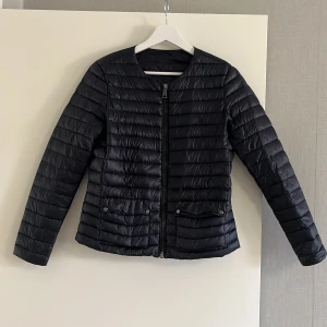 Marinblå  pufferjacka från Ralph Lauren - Snygg mörkblå marin pufferjacka från Ralph Lauren med diskret broderad logga på bröstet. Jackan har raka kanaler, dragkedja framtill och två fickor med knappstängning. Tillverkad i glansigt material som ger en modern look.priset kan diskuteras 