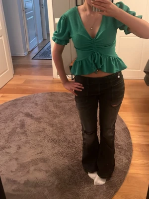 Grön croppad topp med puffärm - Snygg grön croppad topp med puffärmar och v-ringning. Toppen har knyt i midjan och volangkant nedtill som ger en feminin touch. Perfekt för dig som gillar trendiga detaljer och vill sticka ut lite extra.