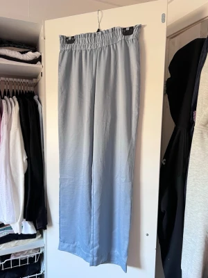 Ljusblå vida satin-pyjamasbyxor med resårmidja, stl S - Säljer ett par ljusblå satinbyxoe med bred resår i midjan och raka, vida ben. Materialet är svalt och stilrent.