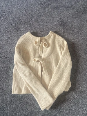 Beige stickad kofta från Object - Supersöt beige stickad kofta från Object med ribbad struktur och två knytband framtill. Koftan har rund halsringning och långa ärmar, perfekt för lager på lager och en clean look.