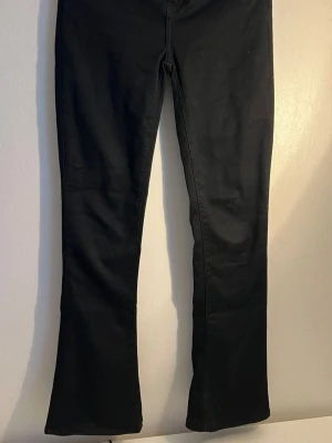 Svarta bootcut jeans - Snygga svarta bootcut jeans med klassisk femficksdesign och utsvängda ben. Jeansen har en enkel look utan synliga loggor och är tillverkade i ett stretchigt material som sitter bekvämt. Perfekta för dig som gillar en tidlös och clean stil.
