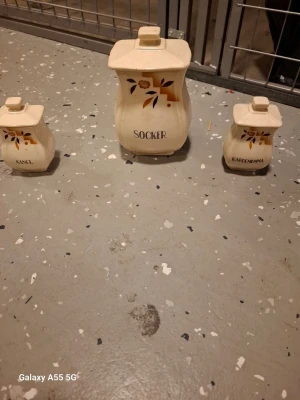 Keramiska burkar för kryddor och socker - Set med tre vintage-inspirerade keramiska burkar med lock, märkta 'Socker', 'Kanel' och 'Kardemumma'. Burkarna är cremefärgade med handmålat blommönster i brunt och orange. Perfekta för förvaring av kryddor och socker i köket.