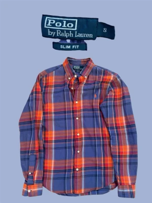 Rutig skjorta från Polo Ralph Lauren - Snygg rutig skjorta från Polo Ralph Lauren i blått och rött med orange detaljer. Skjortan har lång ärm, knappar framtill och klassisk krage. Slim fit-modell som sitter tajt och stilrent. Perfekt för dig som gillar färg och mönster.