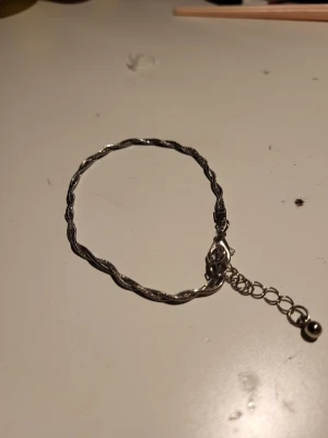 Silvrigt tvinnat armband - Snyggt armband i silverfärg med tvinnad design och justerbar kedja med liten kula i änden. Perfekt accessoar för dig som gillar stilrena och trendiga smycken. Passar till många olika looks och är lätt att matcha med andra armband.