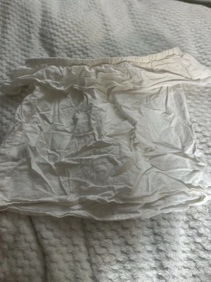 Vit axelbandslös bandeau topp - Säljer en enkel vit bandeau topp med resår upptill. Toppen är axelbandslös och har en luftig passform, perfekt för varma dagar. Tillverkad i ett tunt och mjukt material som känns skönt mot huden.