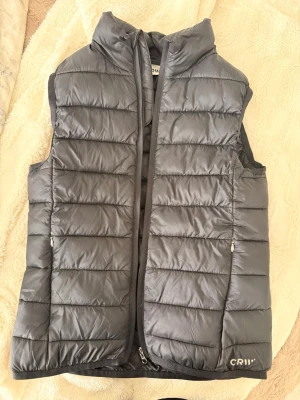 Svart dunväst från CRW💗 - Snygg svart dunväst från CRW i storlek barn 158/164 med hög krage och dragkedja framtill. Västen har två sidofickor med dragkedja. Den är normal i storleken och i bra skick 🤗Kan skicka fler bilder om det önskas ☺️