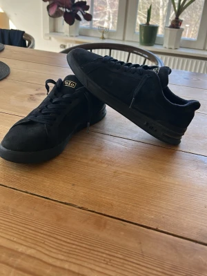 Svarta Polo Ralph Lauren sneakers - Stilrena mörkblåa sneakers från Polo Ralph Lauren i mocka med mörkblå sula och mörkblåa skosnören. Klassisk låg modell med diskret logga på plösen. Perfekta för dig som gillar en clean och enkel look.