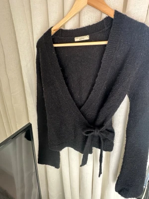 Svart omlottkofta från Gina Tricot - Säljer en svart stickad omlottkofta från Gina Tricot. Koftan har långa ärmar, bred ribbad kant och knyts i midjan med ett band. Tröjan är lite nopprig 💕