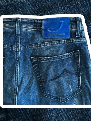 B Jacob Cohen jeans - Säljer ett par blå jeans från Jacob Cohen med snyggt slitna detaljer och klassisk femficksmodell. Jeansen har en rak passform och en blå patch med logga bak i midjan. Perfekta för en avslappnad och trendig look.