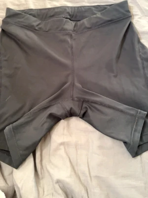 Svarta tighta träningsshorts - Säljer ett par svarta, tighta träningsshorts i stretchigt material. De har en bred midja och slimmad passform som sitter skönt vid träning eller sport. Perfekta för gymmet eller löprundan!