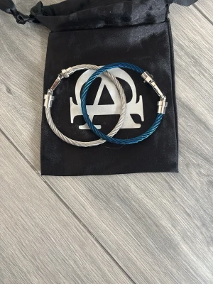 Två stilrena armband i stål - Säljer två snygga armband från All cap one, ett i blått 🔵 och ett i silverfärgat stål 🪙. Båda har en tvinnad wire-design och coola magnetlås 🧲 i metall. Perfekta accessoarer för dig som gillar en modern och industriell look och även perfekt till sommaren då de är ljusa färger och du vill sticka ut ☀️⛱️. Levereras i originalpåse med allcap1-logga.   Köptes för 250kr - mitt pris 149kr helt oanvända. Säljes pga att de var för stora