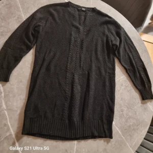 Svart stickad tröja med flätmönster - Säljer en svart stickad tröja med snyggt flätmönster längs mitten fram. Tröjan har rund halsringning, långa ärmar och ribbade muddar vid ärmslut och nederkant. Perfekt för dig som gillar enkel men stilren design.