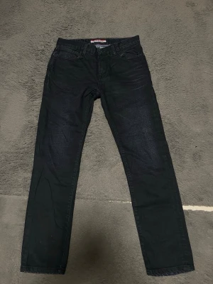 Svarta jeans från Tommy Hilfiger - Snygga svarta jeans från Tommy Hilfiger med klassisk design och logga på bakfickan. Jeansen har en slim design och är tillverkade i ett slitstarkt denimtyg som passar perfekt till en trendig vardagslook. Storlek 30x30