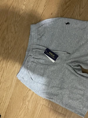 Grå mjukisbyxor från Polo Ralph Lauren - Snygga grå mjukisbyxor från Polo Ralph Lauren med klassisk logga broderad på höften. Byxorna har dragsko i midjan och är tillverkade i mjukt bomullsmaterial. Perfekta för en chill och avslappnad stil.
