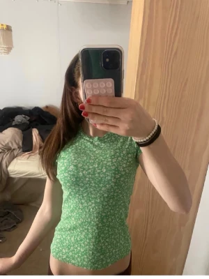 Sommar topp - Grön ribbad topp med små vita blommor och tight passform. Kortärmad modell med rund halsringning, perfekt för vår och sommar. Superfin att styla med jeans eller kjol! Hör av dug för frågor❣️