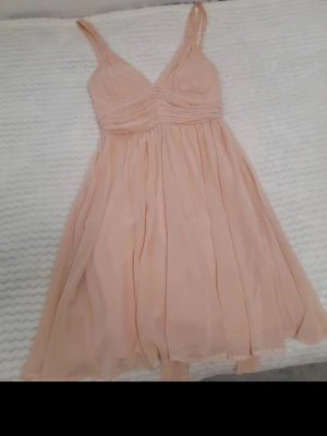 Ljusrosa omlottklänning med volang - Söt ljusrosa kortklänning med omlottdesign och tunna axelband. Klänningen har volangdetaljer och ett luftigt, svepande tyg som ger en romantisk känsla. Perfekt för sommarens alla tillfällen.