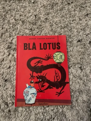 Blå Lotus - Tintins äventyr - Säljer seriealbumet 'Blå Lotus' från Tintins äventyr av Hergé. Boken har ett rött omslag med en svart drake, kinesisk lykta och Tintin i blå kimono. Baksidan har färgglad illustration med flera karaktärer. Perfekt för Tintin-fans och samlare.