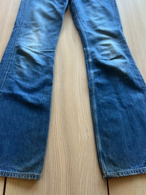 Blå bootcut jeans i denim - Snygga blå bootcut jeans i klassisk denim med lätt slitning vid knäna. Jeansen har raka ben och en tidlös tvätt som passar till många olika stilar. Perfekta för dig som gillar en avslappnad och trendig look.