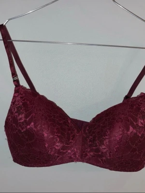 Vinröd spets-bh från Lindex Flirt - Vinröd bh från Lindex Flirt-kollektion med vacker spets och vadderade kupor. Bh:n är bygel- och sömlös för extra komfort och har justerbara axelband. Perfekt för dig som vill ha en snygg och bekväm bh med medelhög täckning.