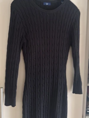 Svart stickad klänning Gant - Marinblå stickad klänning från Gant med kabelstickat mönster. Klänningen har lång ärm, rund halsringning och en tight passform. Perfekt för dig som gillar en klassisk och enkel stil. Strl XS