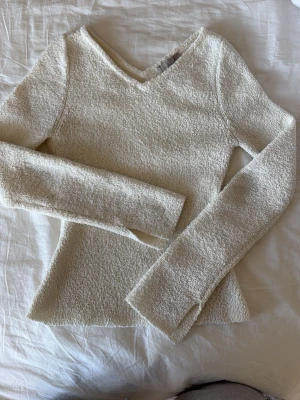 Vit stickad tröja med v-ringning - Säljer en krämvit stickad tröja med v-ringad hals och långa ärmar. Tröjan har en lätt figurnära passform och är gjord i ett mjukt, strukturerat material som känns skönt mot huden. Perfekt att styla med jeans eller kjol för en enkel och snygg look.