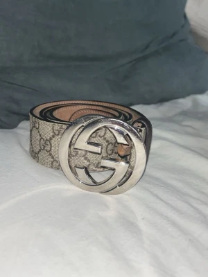 Gucci GG beige bälte äkta har  kvitto  - Snyggt beige bälte från Gucci med klassiskt GG-mönster och stor silverfärgad GG-spänne. Bältet har en lyxig känsla och passar perfekt till jeans eller kostymbyxor. Materialet är skinn med canvas-yttermaterial och ikoniskt Gucci-tryck. Har kvitto att det är äkta  