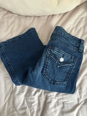 Mörkblå jeans med fickdetalj - Snygga mörkblå jeans med klassisk femficksdesign och en markerad ficka bak med knapp. Jeansen har bootcut ben och tydliga sömmar. Perfekt för en trendig look.
