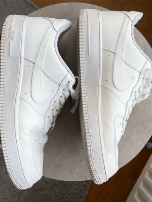 Nike Air Force 1 vita sneakers - Klassiska helvita Nike Air Force 1 sneakers med lågt skaft. Skorna har en chunky sula, perforerade detaljer på tån och ikoniska swoosh-loggan på sidorna. Tillverkade i läder med textilfoder och snörning framtill. Perfekta för en clean och stilren look. Bra skick och inte mycket tecken på användning. Storlek 45 pris kan diskuteras